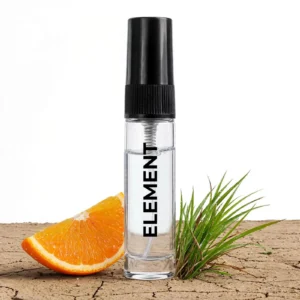 CocoBerry Element 5ml tester perfume bottle resting on dry cracked earth with a fresh orange slice and green grass.