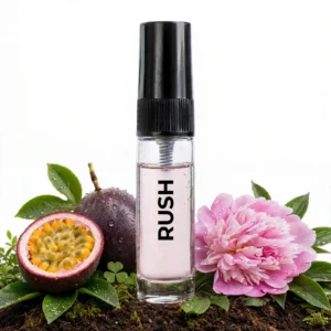 CocoBerry Rush 5ml tester perfume bottle displayed on dark soil alongside a freshly cut passionfruit and a large pink peony flower.