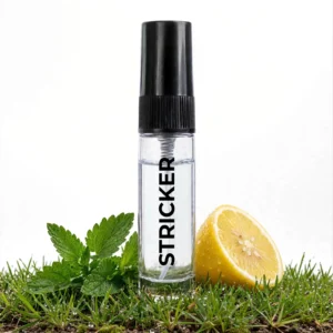 CocoBerry Stricker 5ml tester perfume bottle resting on fresh green grass alongside a cut lemon and green mint leaves.