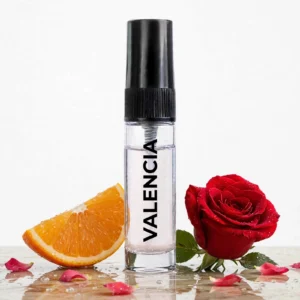 CocoBerry Valencia 5ml tester perfume bottle placed on a wet surface with a fresh orange slice, a vibrant red rose, and scattered rose petals.